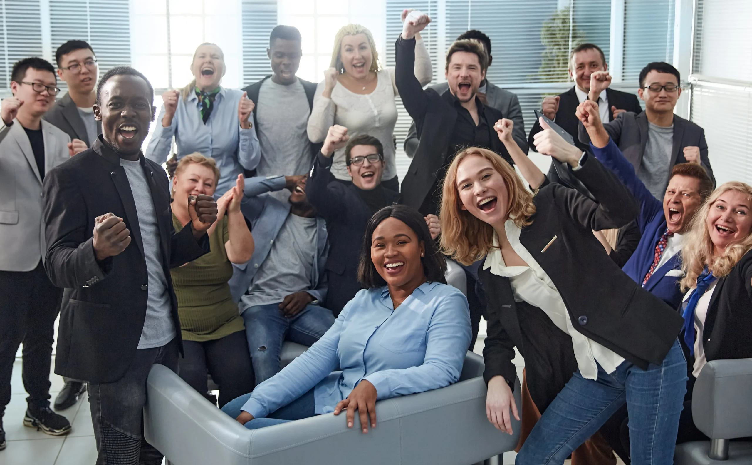 Group of coworkers cheering in an office, symbolizing team success and a positive workplace culture.