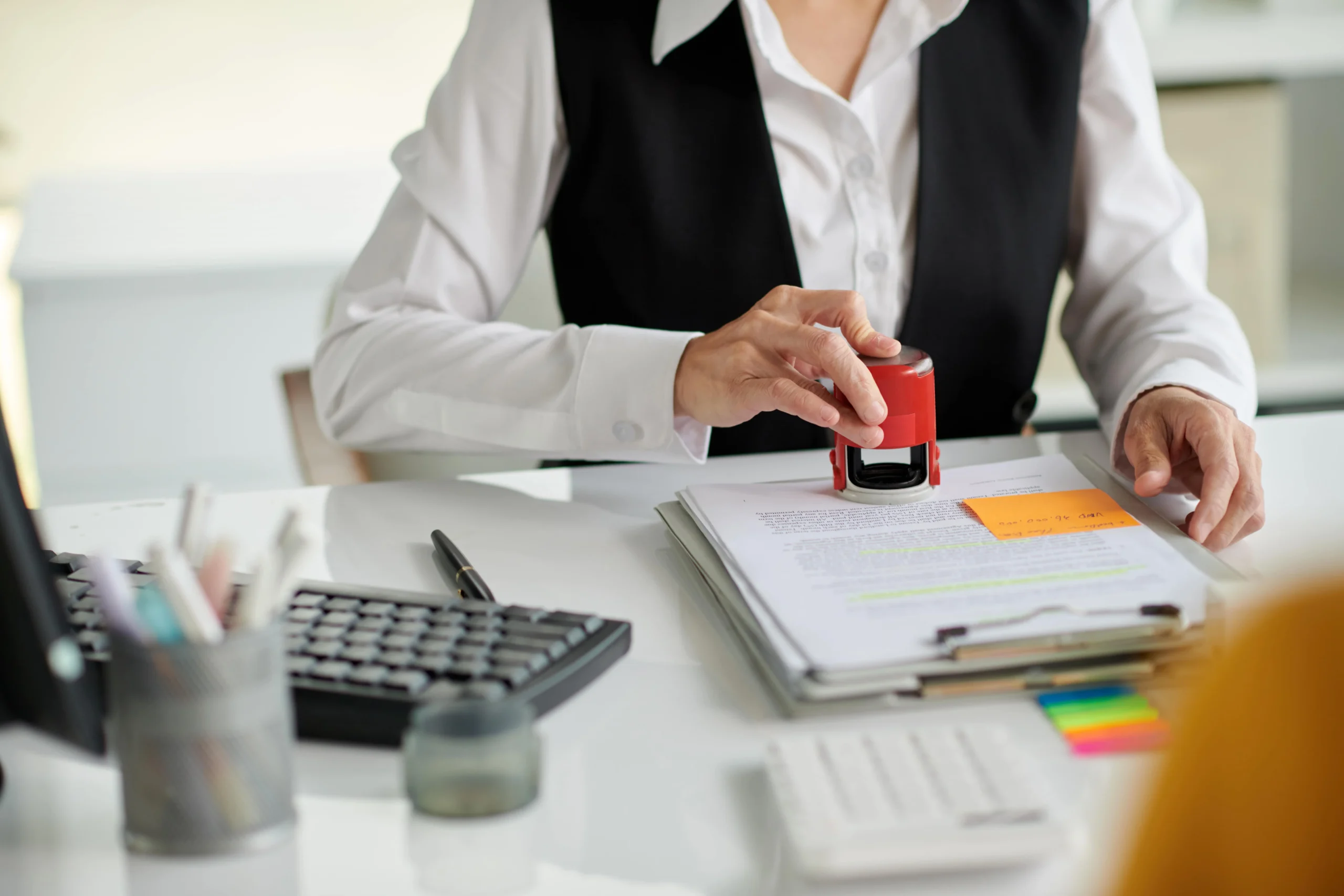 Employee stamping official documents on a desk with office supplies.