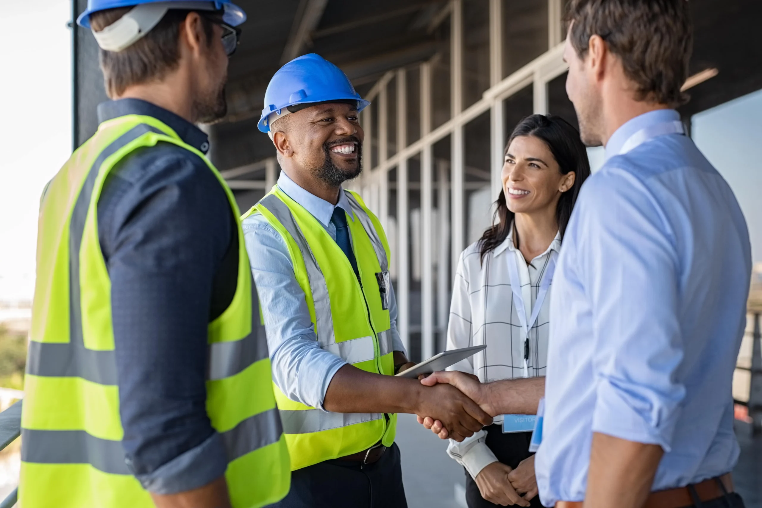 Construction manager shaking hands with a worker in safety gear at a building site, with another team member nearby.