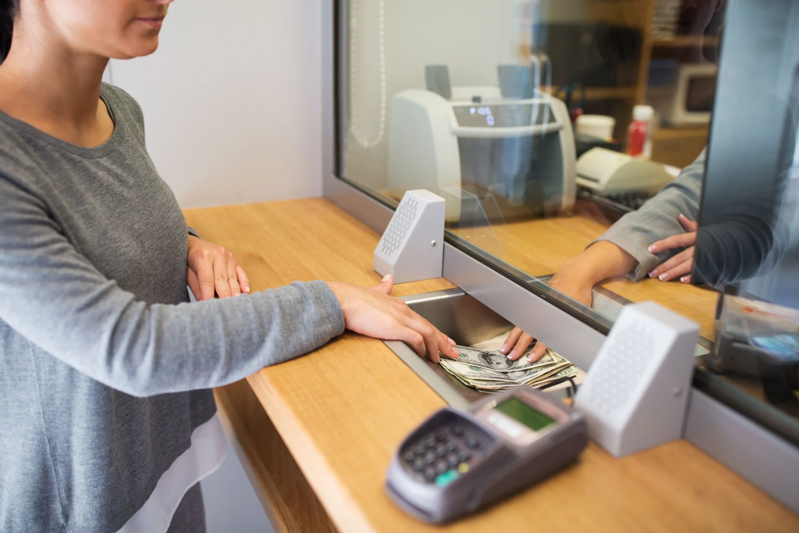 Person completing a cash transaction at a teller counter with a payment terminal and currency notes visible.